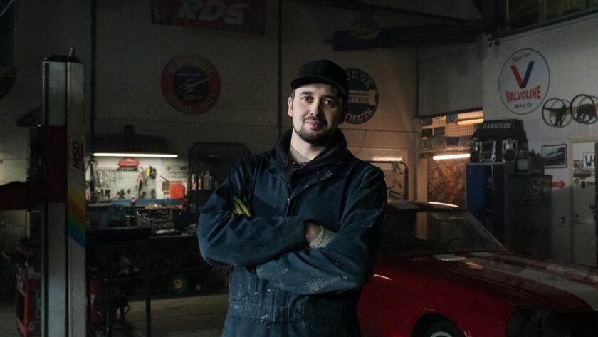 Mécanicien heureux dans un garage travaillant sur la restauration d’une voiture classique.